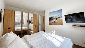 A bedroom with a bed, a TV mounted on the wall, and a wooden wardrobe. - Apartment 02 with fireplace & terrace - A: Haus Strandkiefer - close to the beach (Baabe)