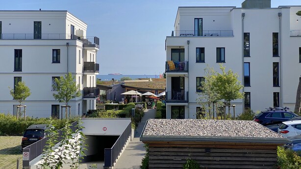 A modern residential building with balconies, a covered outdoor seating area, and a view of the sea. - Apartment 02 with fireplace & terrace - A: Haus Strandkiefer - close to the beach (Baabe)