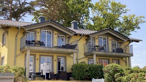 A yellow building with two balconies, a signboard, and a garden with flowers. - Apartment 02 with fireplace & terrace - A: Haus Strandkiefer - close to the beach (Baabe)
