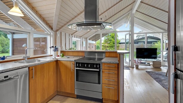 Een moderne keuken met houten kasten, een roestvrijstalen fornuis en een groot raam met uitzicht op een tuin.