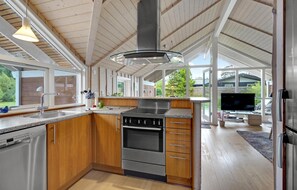 Eine moderne Küche mit Holzschränken, einem Edelstahlherd und einem großen Fenster mit Blick auf einen Garten.