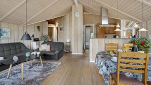 Een ruime woonkamer met een bank, salontafel en een eettafel gedekt voor twee personen. In de achtergrond is een keuken te zien met moderne apparatuur.