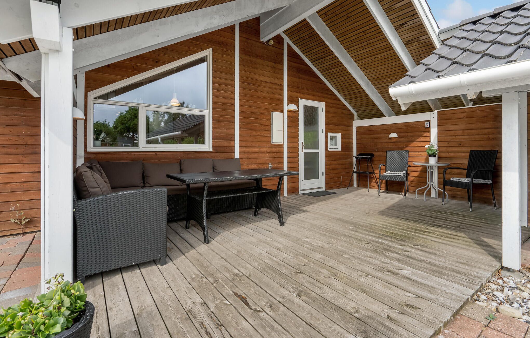A covered outdoor area with a wooden deck, a seating area with a table and chairs, and a door leading to an interior space.