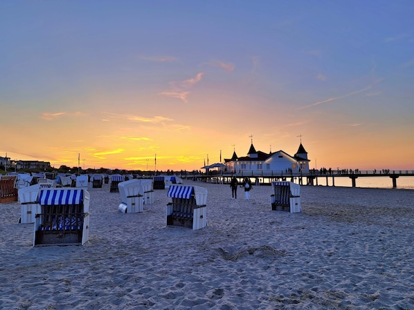Ein Strand mit Liegen und Sonnenschirmen, ein Steg und ein Gebäude mit einem Turm.