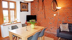 A dining area with a wooden table, chairs, a TV, and a brick wall.