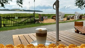 A table with a drink and pastries, a wooden fence, and a view of a body of water and hills.