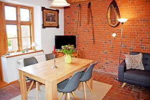 Comedor con una mesa de madera, sillas, televisor y pared de ladrillo.