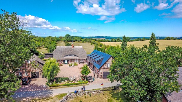 A traditional half-timbered house with a thatched roof, surrounded by lush greenery and a clear blue sky.