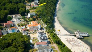 Vista aerea di una cittadina costiera con spiaggia, molo e diversi edifici, tra cui hotel e abitazioni.