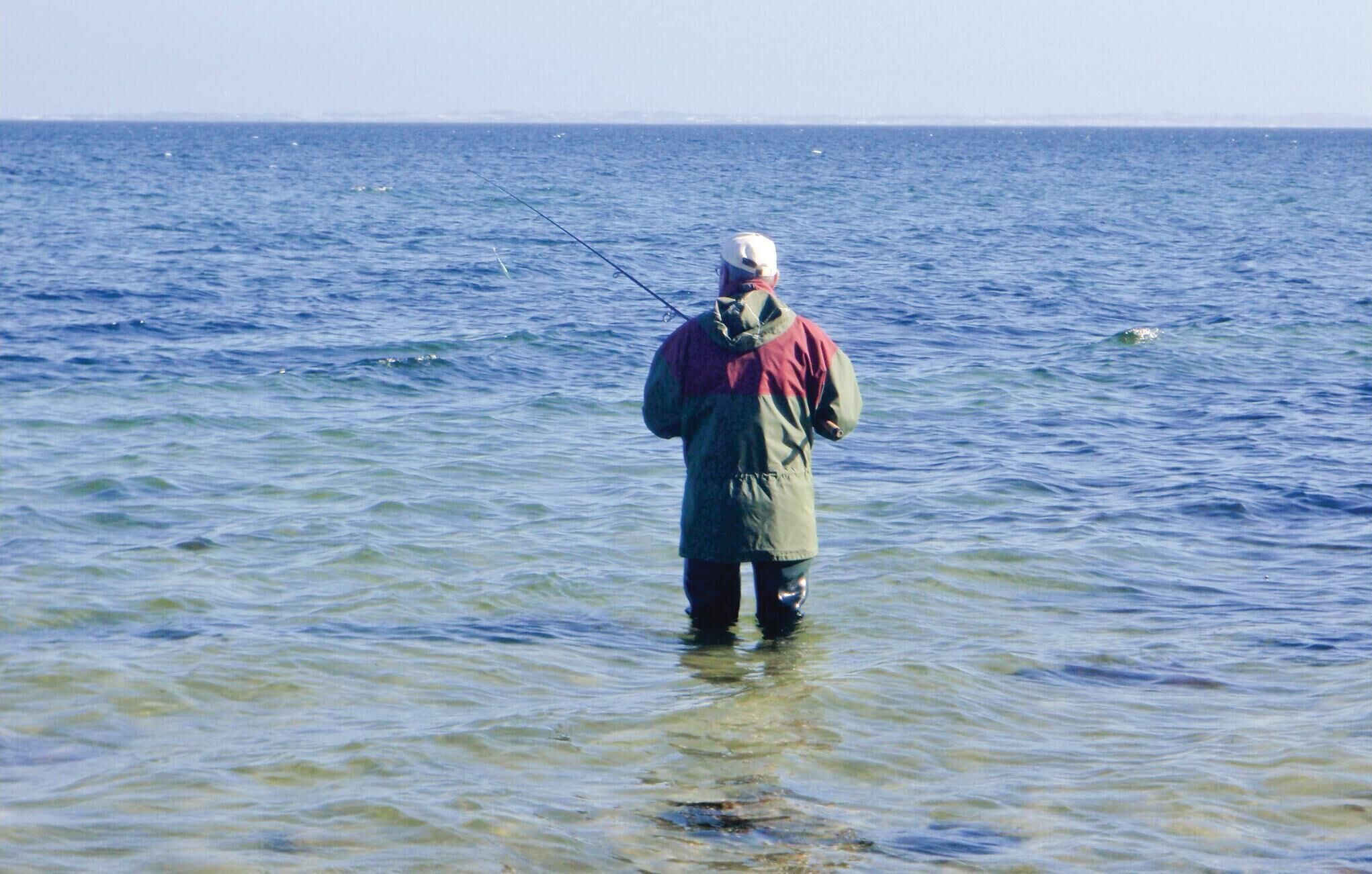 En person står i lavt vand med fiskestang.