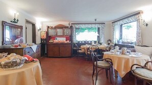 Un espace repas comprenant des tables, des chaises, un buffet et donnant sur l’extérieur.