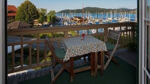Un balcon avec une table, une vue sur une marina avec des bateaux, et une colline au loin.