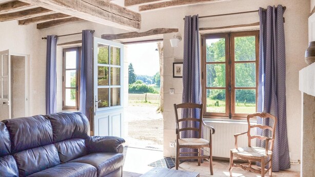 A room with a leather sofa, two wooden chairs, a wooden table, and a large window with curtains. - Amazing home in Cravant les Côteaux (Cravant les Côteaux)