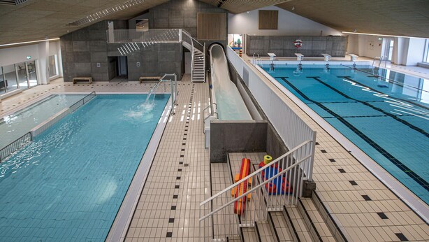 Una piscina interior con varias pistas de natación, un tobogán y una escalera que conduce a un entrepiso.