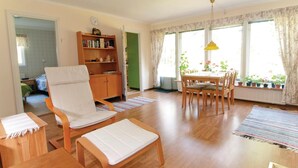 Ein geräumiges Wohnzimmer mit einer Holzsofa, einem Esstisch mit Stühlen, einem Bücherregal und großen Fenstern mit Vorhängen.