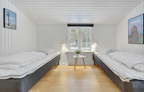 Ein Zimmer mit zwei Einzelbetten, einem kleinen Tisch mit einer Pflanze, einem Fenster mit Blick auf Bäume und zwei gerahmten Bildern an den Wänden.