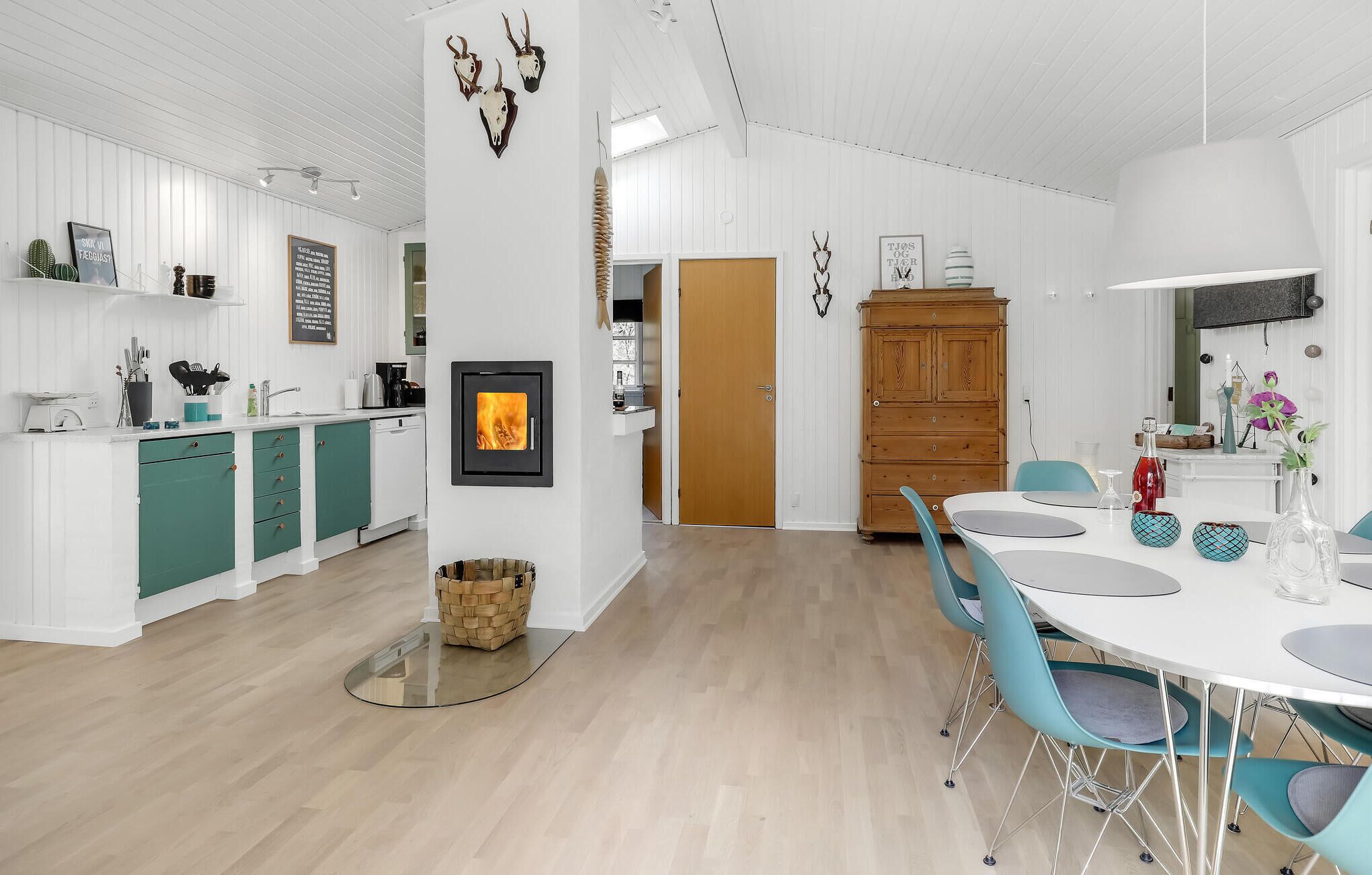 A modern kitchen with a wood-burning stove, teal cabinets, and a dining area with blue chairs and a white table.