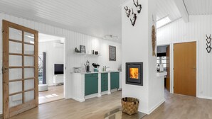 Un'ampia zona giorno con camino, pavimento in legno e una grande cucina a vista con mobili verdi.