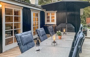 Eine Terrasse im Freien mit einem langen Tisch, Stühlen, einem Grill und einer Laterne.