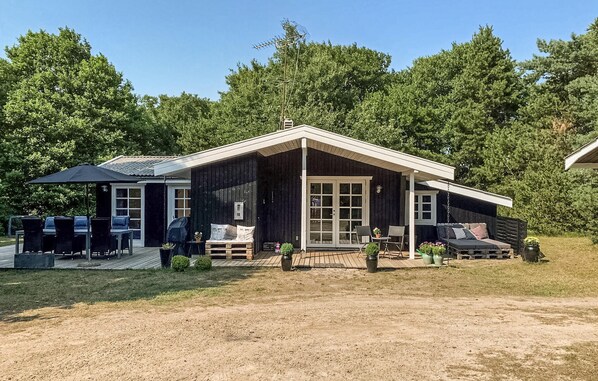 Eine moderne Hütte mit überdachter Terrasse, Sitzgelegenheiten im Freien und einem großen Fenster.