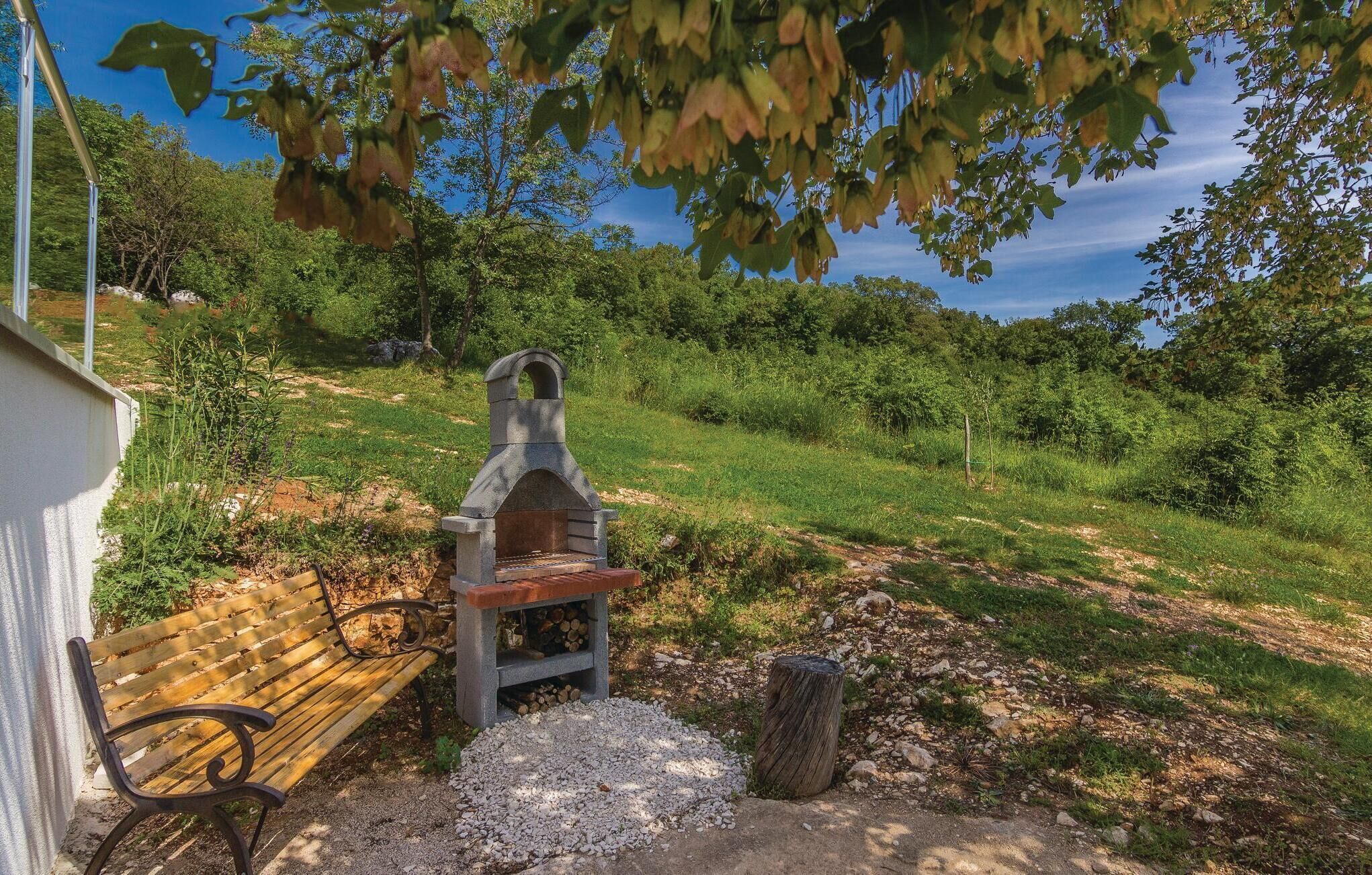 Ein Steingrill mit Sitzbank und einem Baumstumpf in der Nähe.