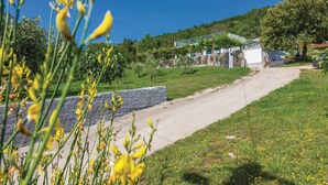 A rural road leading to a white building with a stone foundation, surrounded by greenery and flowering plants. - Gorgeous home in Trget (Trget)