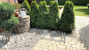 A garden with neatly trimmed hedges, a stone planter with a watering can, and a metal rack.