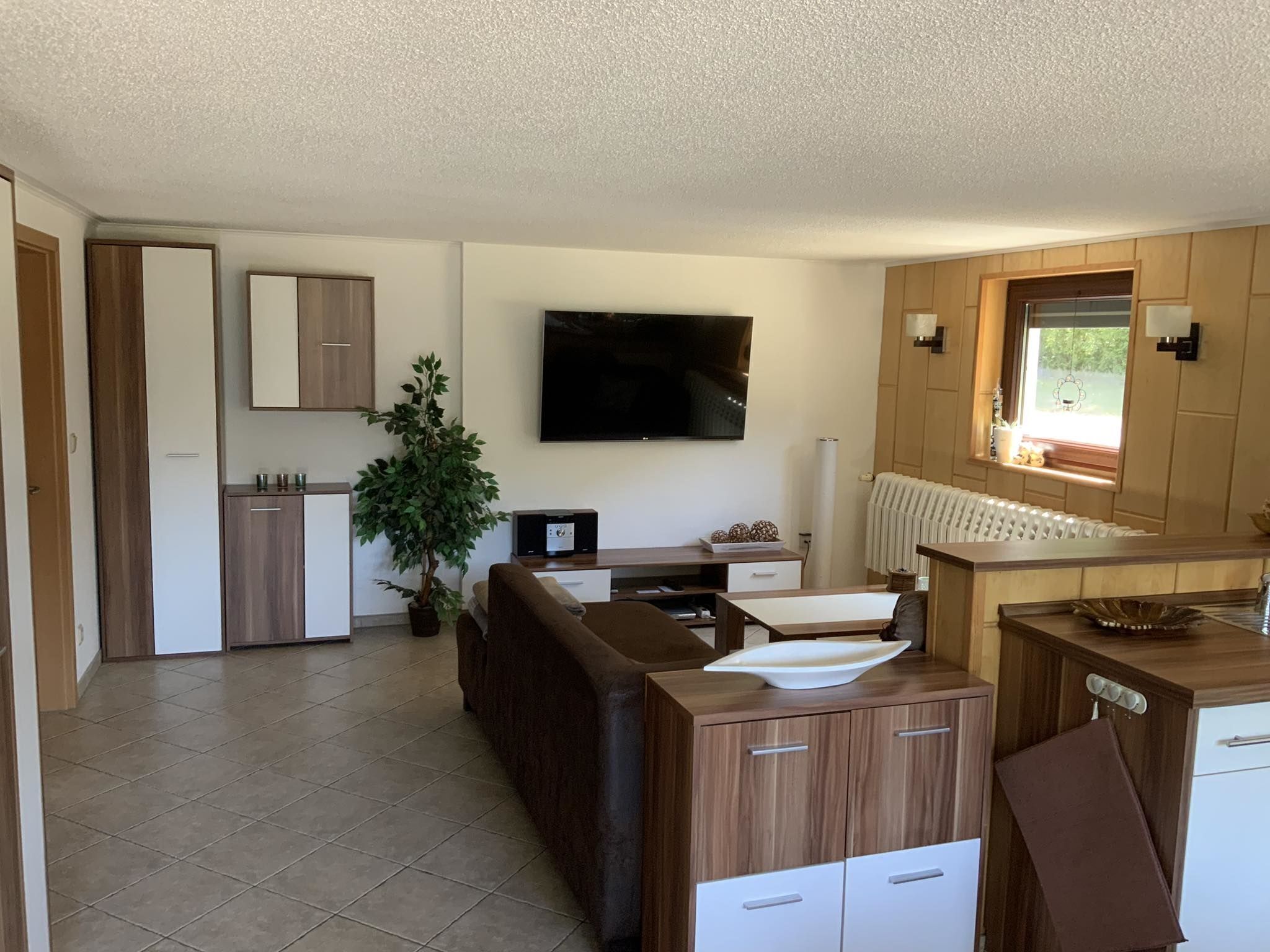 Een moderne keuken met een flatscreen televisie, houten kastjes en een eethoek met een tafel en stoelen.