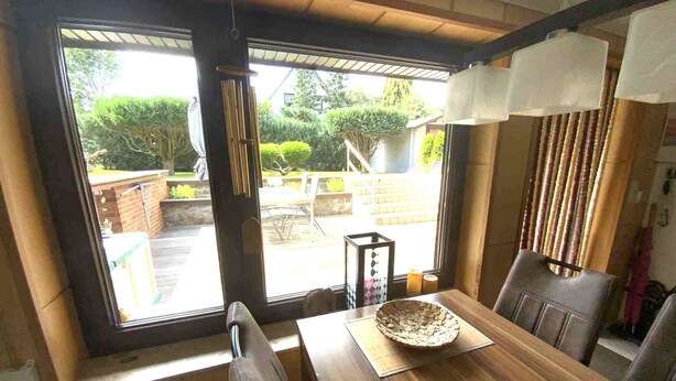 A dining area with a wooden table, chairs, and a view of a garden through a large window.