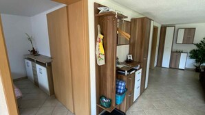 A spacious room with a wooden wardrobe, a small kitchen area, and a tiled floor.