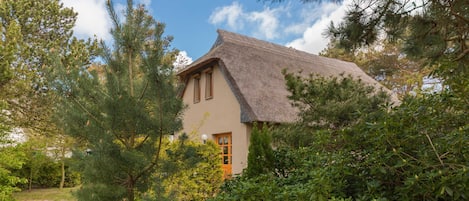 Een huis met rieten dak, omringd door weelderige begroeiing en bomen.