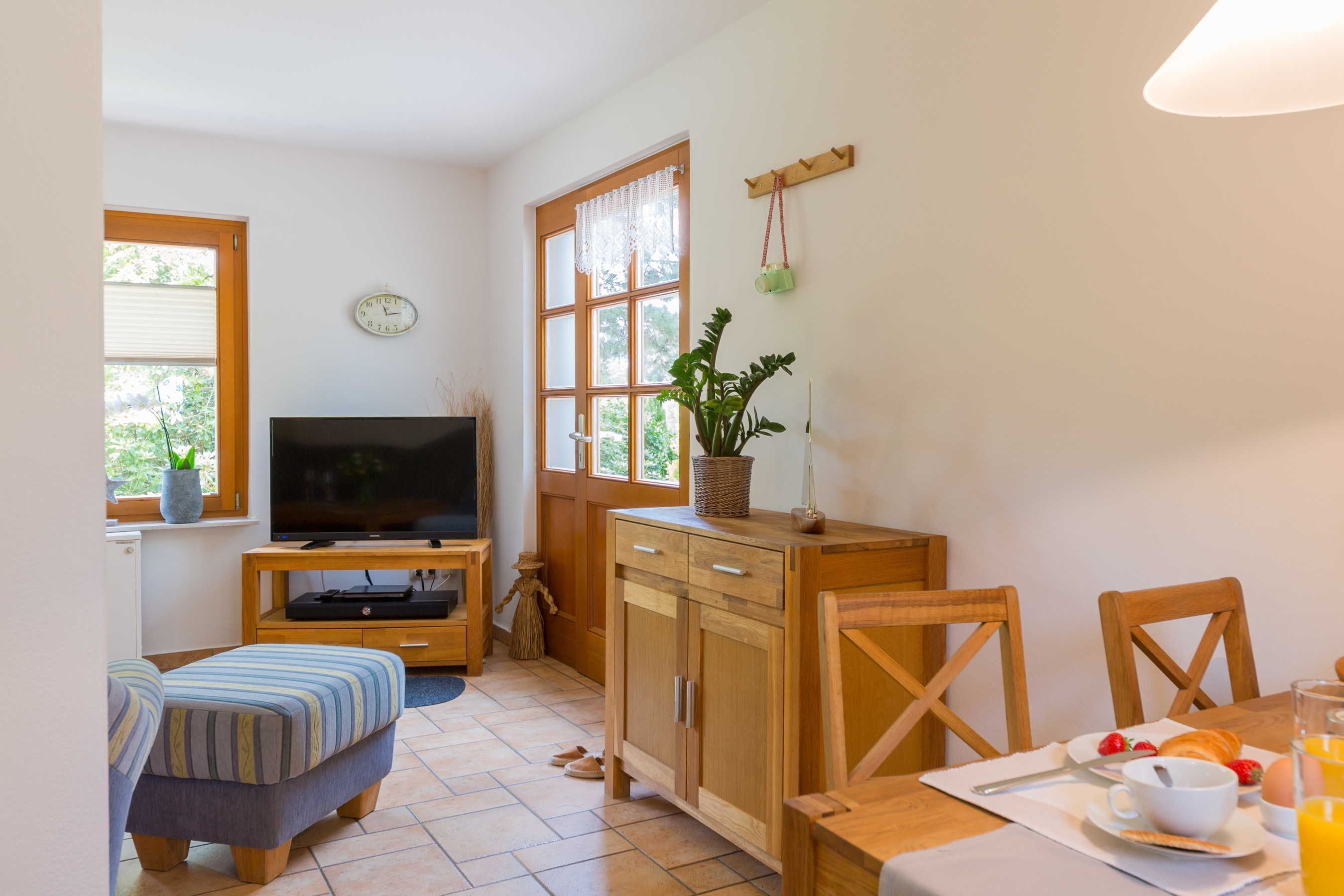A cozy room with a television, wooden furniture, a dining table with breakfast items, and a window with blinds.