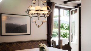 Un comedor con una mesa para dos personas, una araña, un cuadro en la pared y una ventana con vistas a zonas verdes.