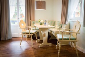 Une pièce avec un plancher en bois, une table entourée de chaises, un banc et une lampe suspendue.