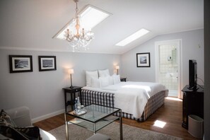A bedroom with a bed, a glass coffee table, a chandelier, a television, and framed pictures on the wall. - EZ Comfort - Bio Design Boutique Hotel Landhaus St. Georg (Bad Wiessee)