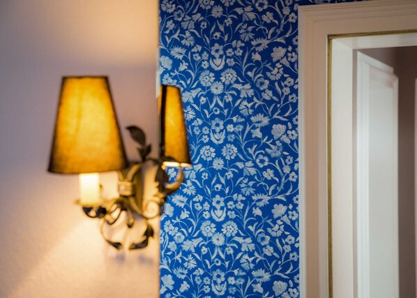 Un luminaire mural avec deux lampes, un papier peint à motifs floraux bleus et un cadre de porte blanc.