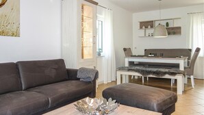 Uma sala de estar moderna com um sofá de couro marrom, uma mesa de centro de madeira e um espaço de jantar com mesa e cadeiras brancas.