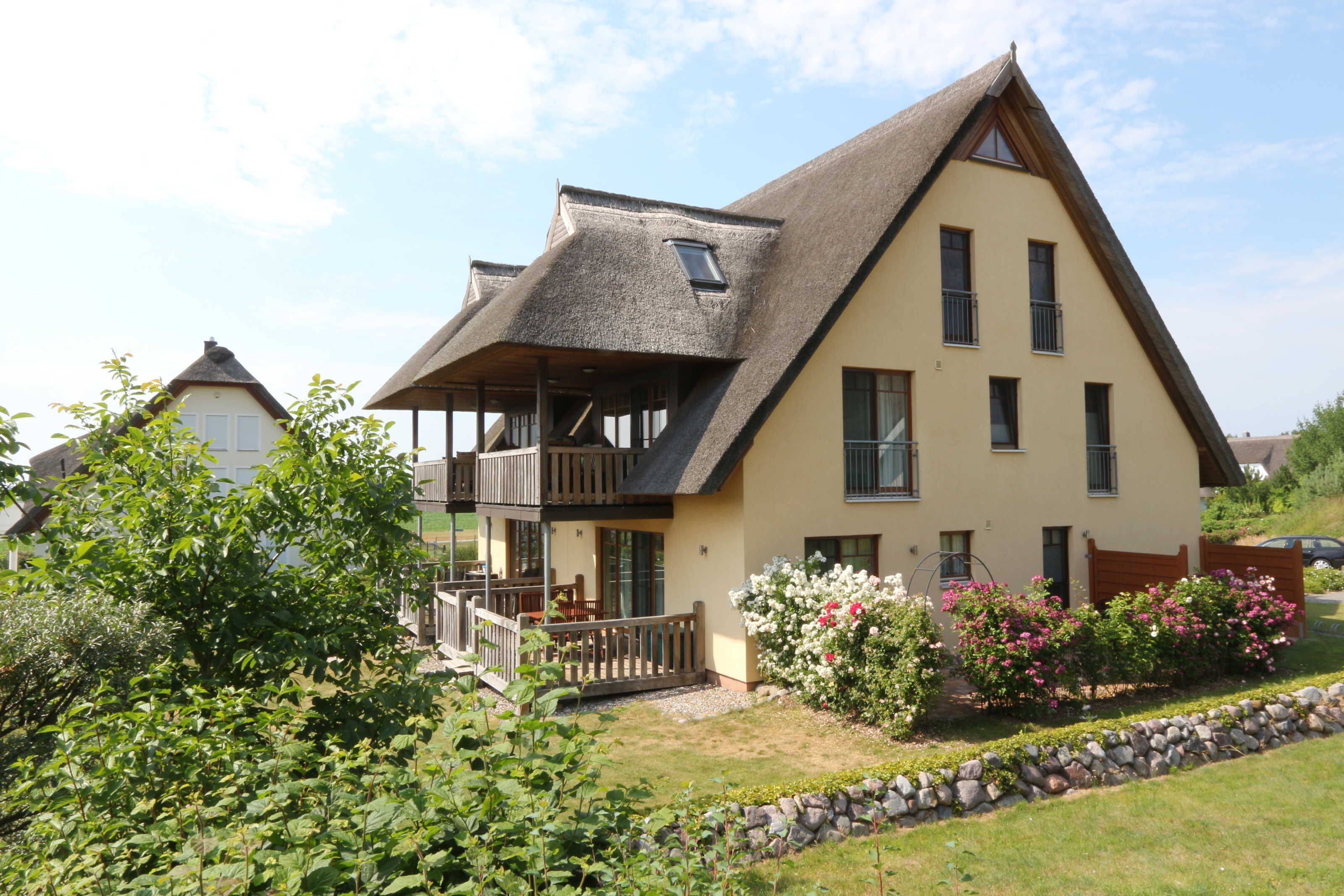 Een tweelaags huis met een schuin dak, een balkon en een tuin vol bloemen.