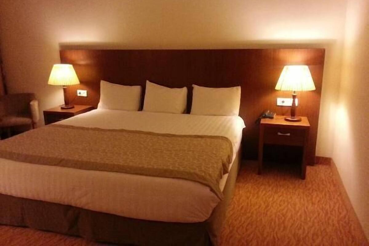 A hotel room with a large bed, two bedside tables with lamps, and a chair.