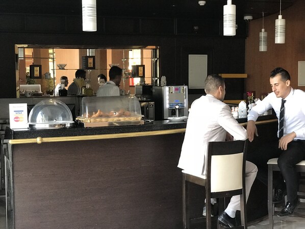 A hotel bar with a counter, a coffee machine, and a buffet display. - Hotel Hocine (El Khroub)