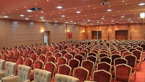 Un salón de conferencias con filas de sillas rojas y beige, paneles de madera y luces de techo.