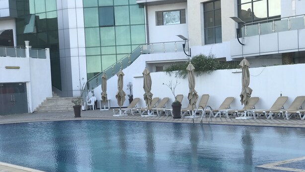 Una piscina con sillones de playa y sombrillas, una escalera y un edificio moderno con ventanas de vidrio.