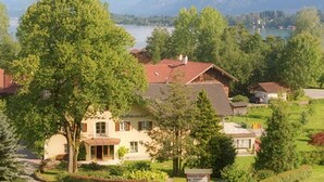 Un albergo con un grande albero di fronte, montagne sullo sfondo e vista sul lago.