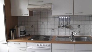 Una cucina con mobili bianchi, un fornello, un forno, un lavello e una macchina da caffè.