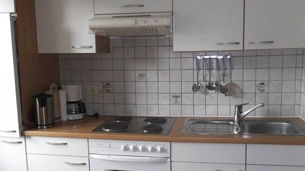 Una cocina con armarios blancos, estufa, horno, pileta y cafetera.