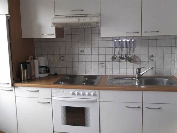 Una cocina con armarios blancos, estufa, horno, pileta y cafetera.
