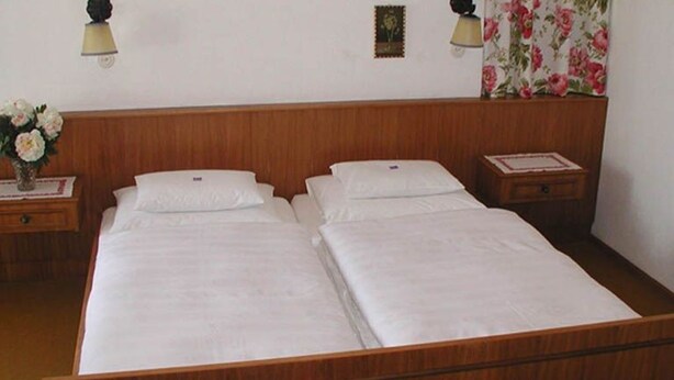 Un letto matrimoniale con testiera in legno, due comodini e una tenda con motivo floreale.