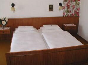Una cama doble con cabecera de madera, dos mesitas de noche y una cortina estampada con motivos florales.