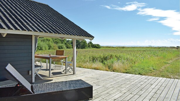 Een houten terras met een overdekte zithoek en uitzicht op een grasveld.