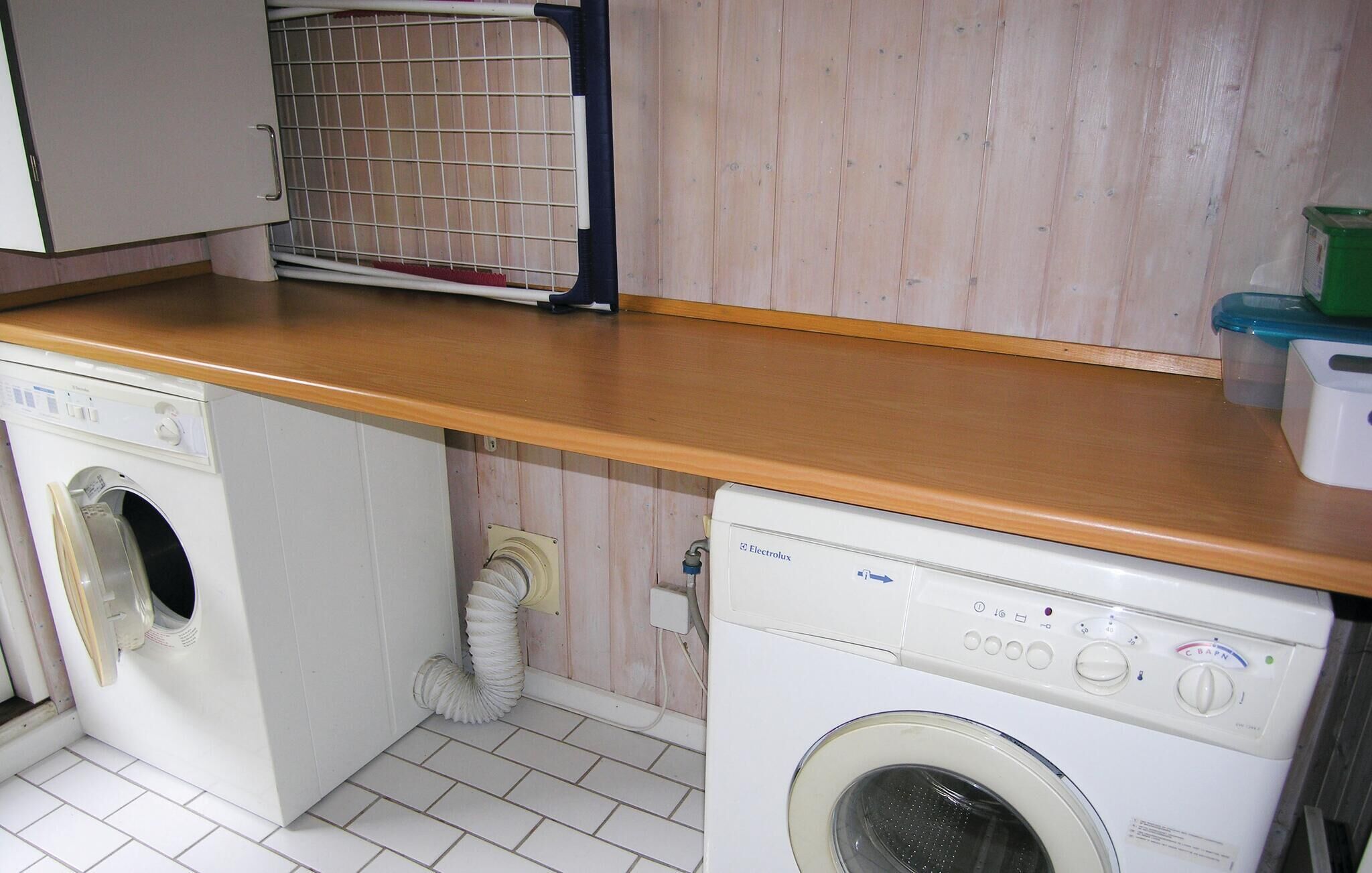 A laundry area with two washing machines, a drying rack, and a wooden countertop.